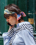 Woman wearing a striped shirt and blue jeans against a green door with a bandana in her hair
